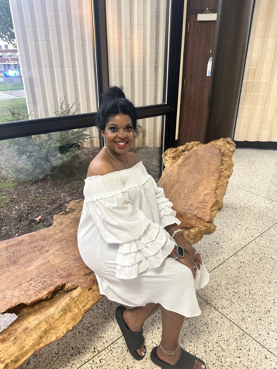 Nadine Martin Jones seated on a natural wood bench, smiling at the camera.